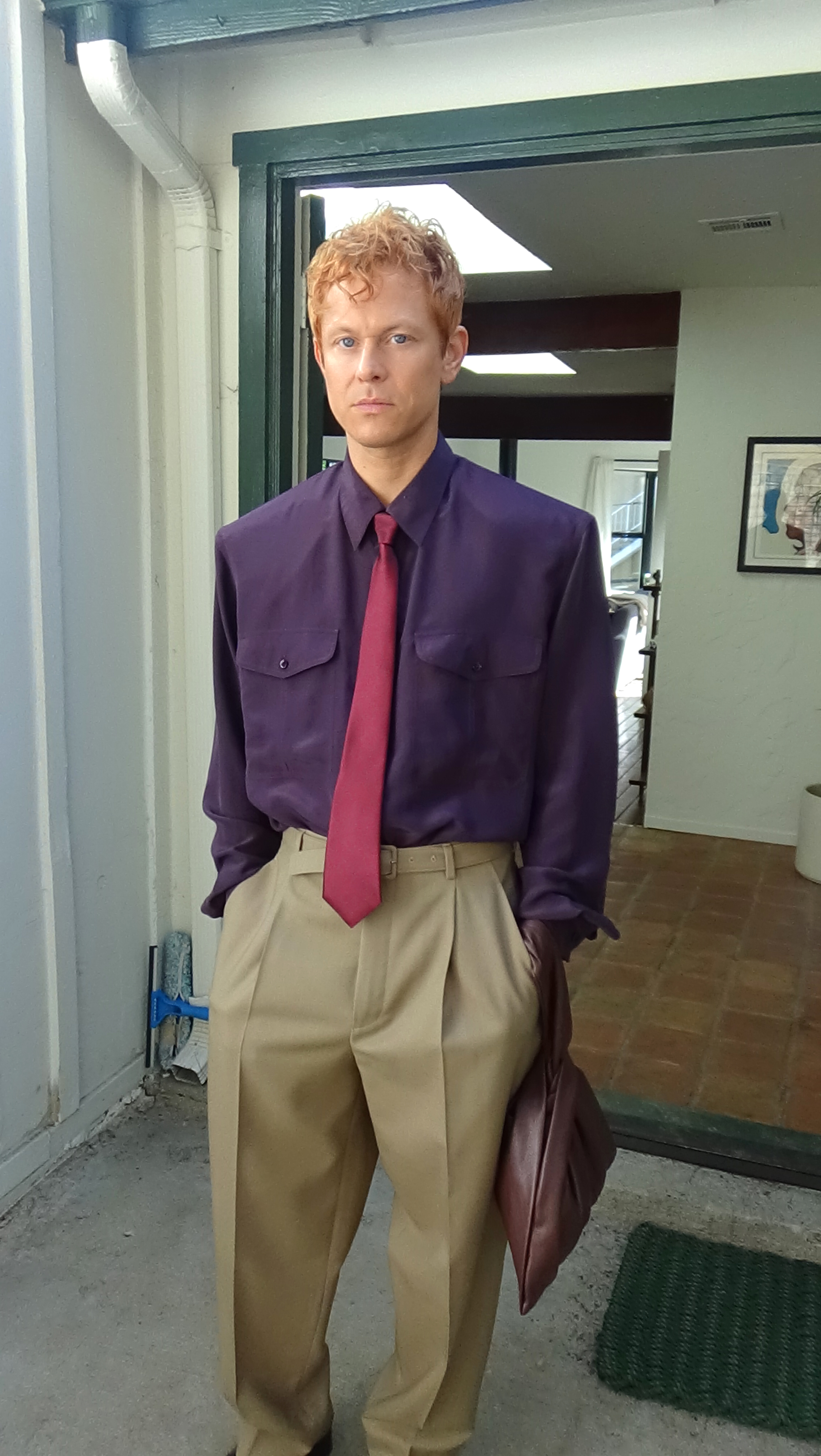 Full body portrait of Mike Hadreas looking at the camera with his hands in his pocket on a sunny patio